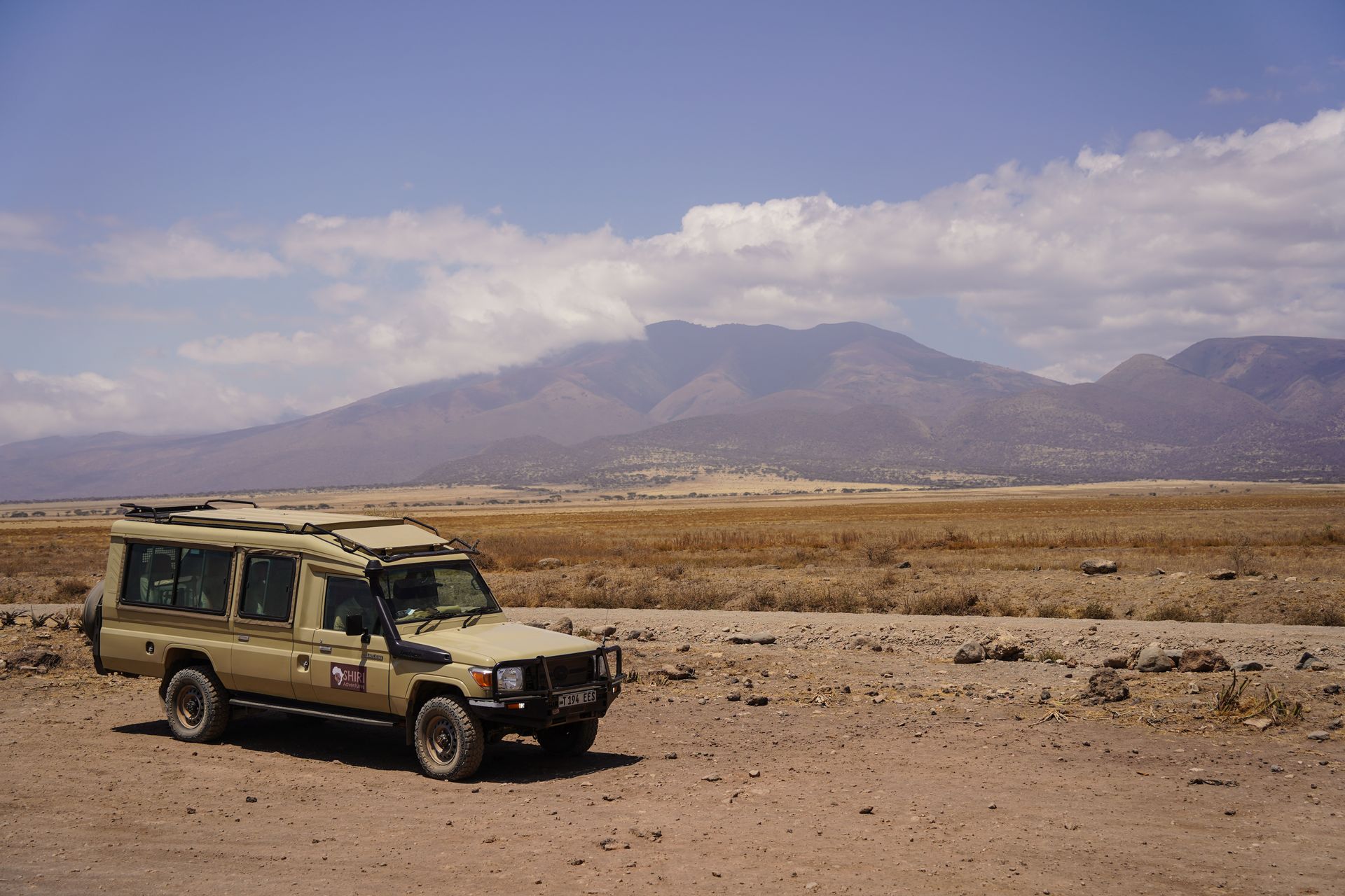 The safari vehicle parked on a dirt road with mountains in the distance