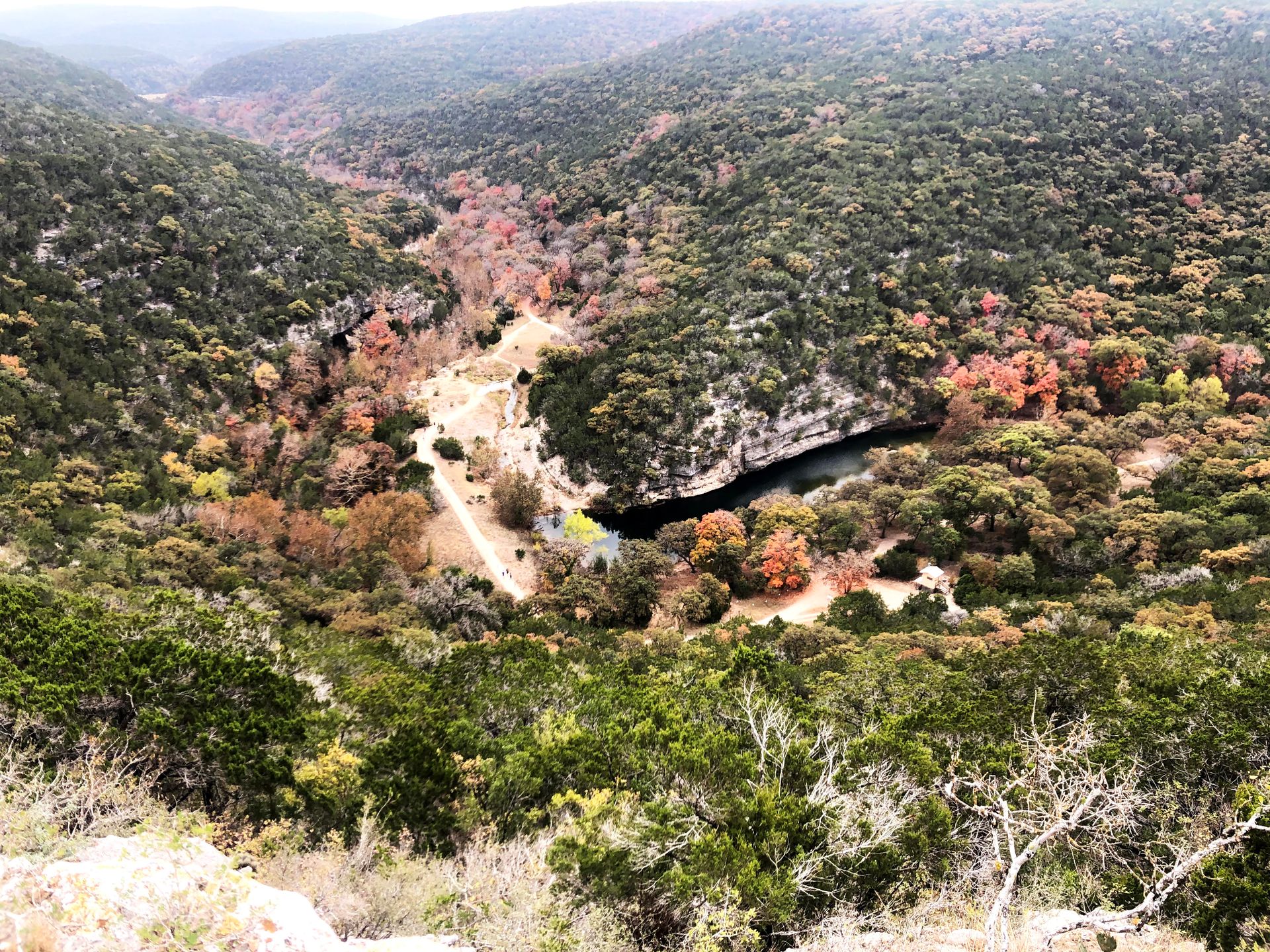 Looking down at the Sabinal River from a hiking trail at Lost Maples. Some trees are red, orange and yellow