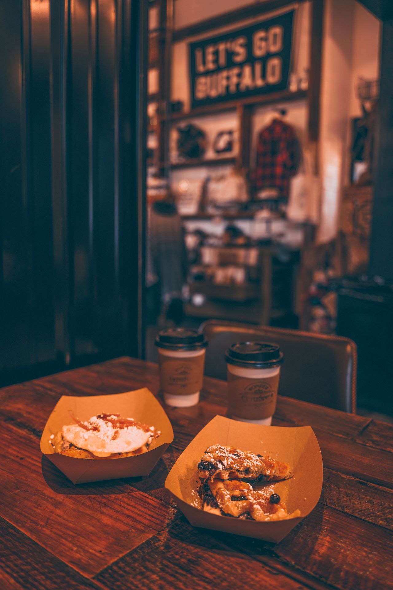 Two waffles on paper plates, along with two coffees inside of Wonder Coffee House.