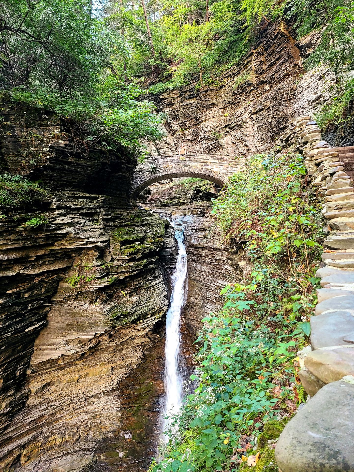 Looking at a waterfall below a stone bridge in the center of a gorge at Watkins Glen.