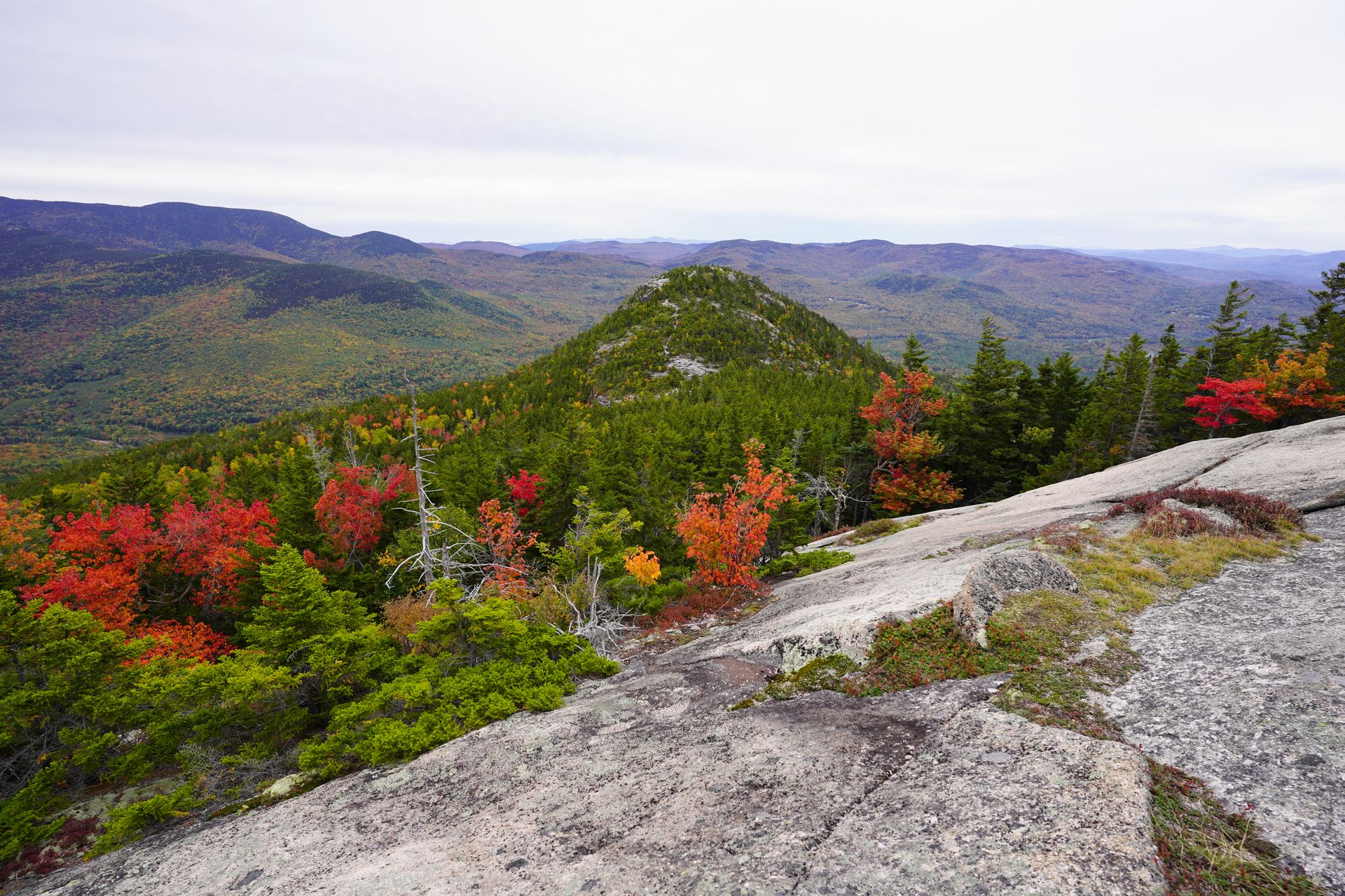 Looking down at the views from the Welch Dickey Loop. There are mountains with mostly green trees with a pops of red.