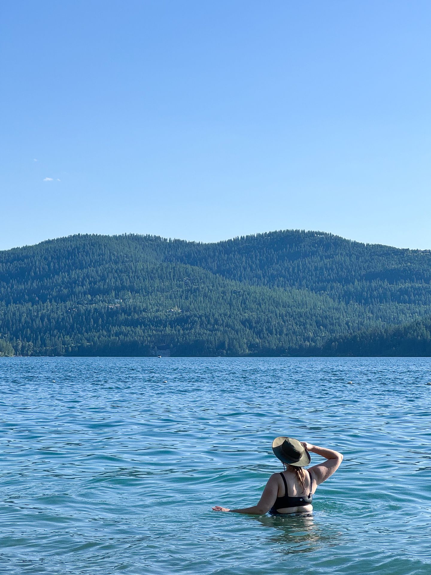 Lydia swimming in Whitefish Lake. There is a hill covered in green trees across the water