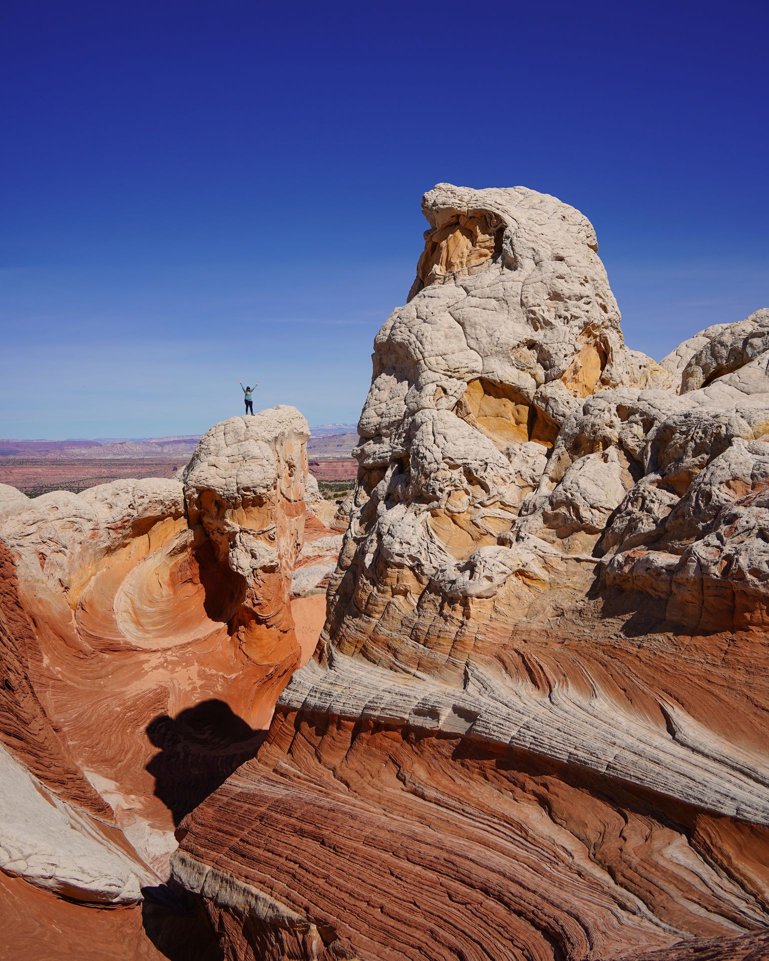 Towering rock formations that are white with swirls of orange. Lydia is standing on a rock in the distance.
