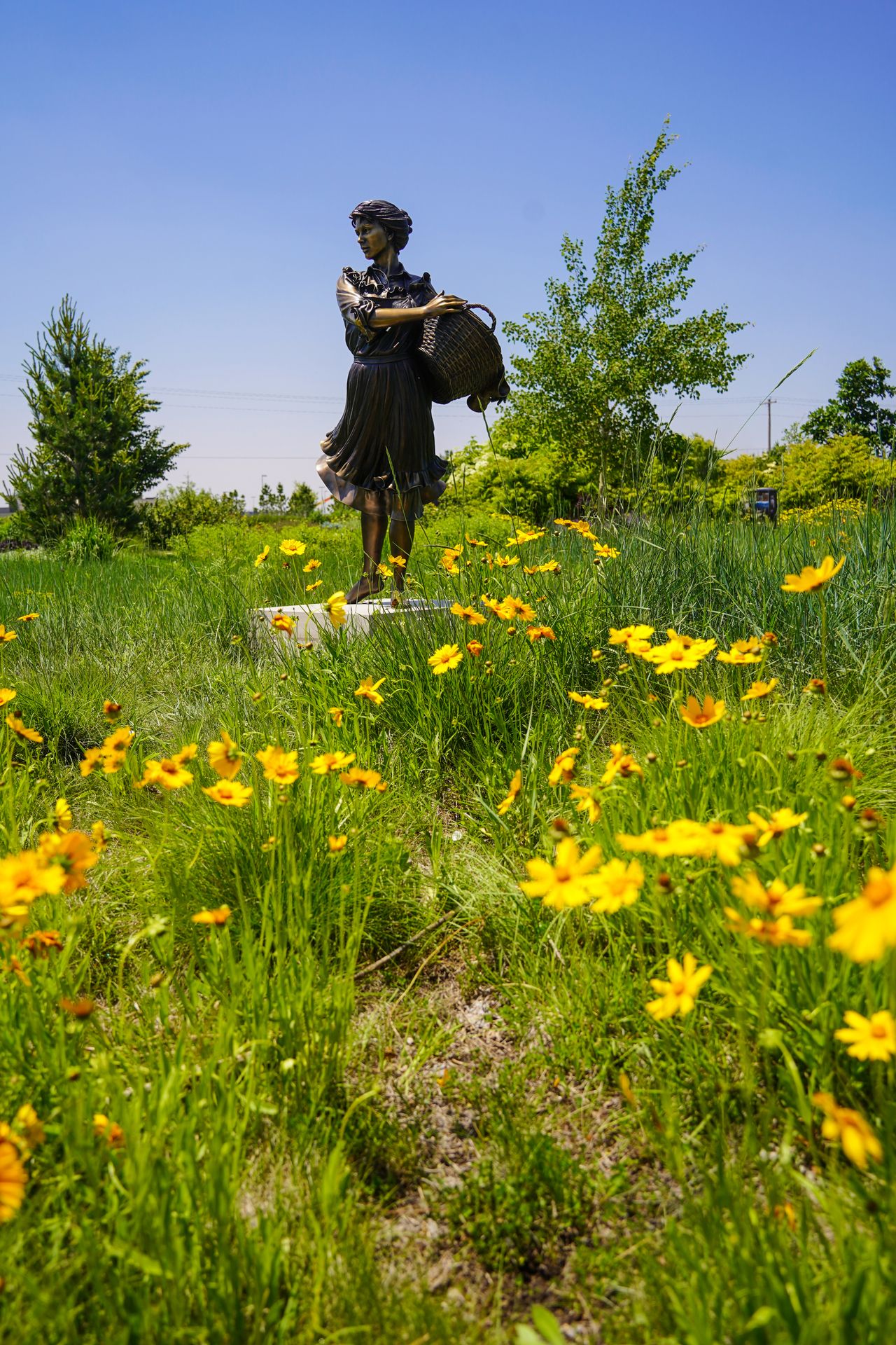 Yellow flowers in front of a statue that features a woman holding a basket.